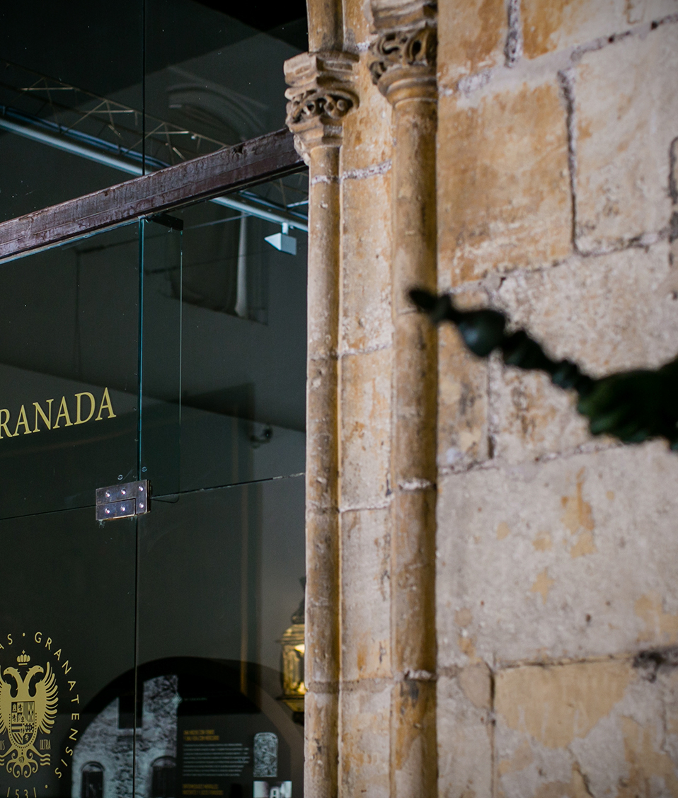 Detalle puerta de cristal del Hospital Real junto a estatua donde se aprecia el logo de la Universidad de Granada en la puerta y parte de la estatua